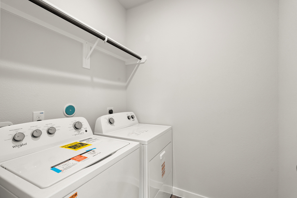 A white laundry room with a white shelf and a white wall.