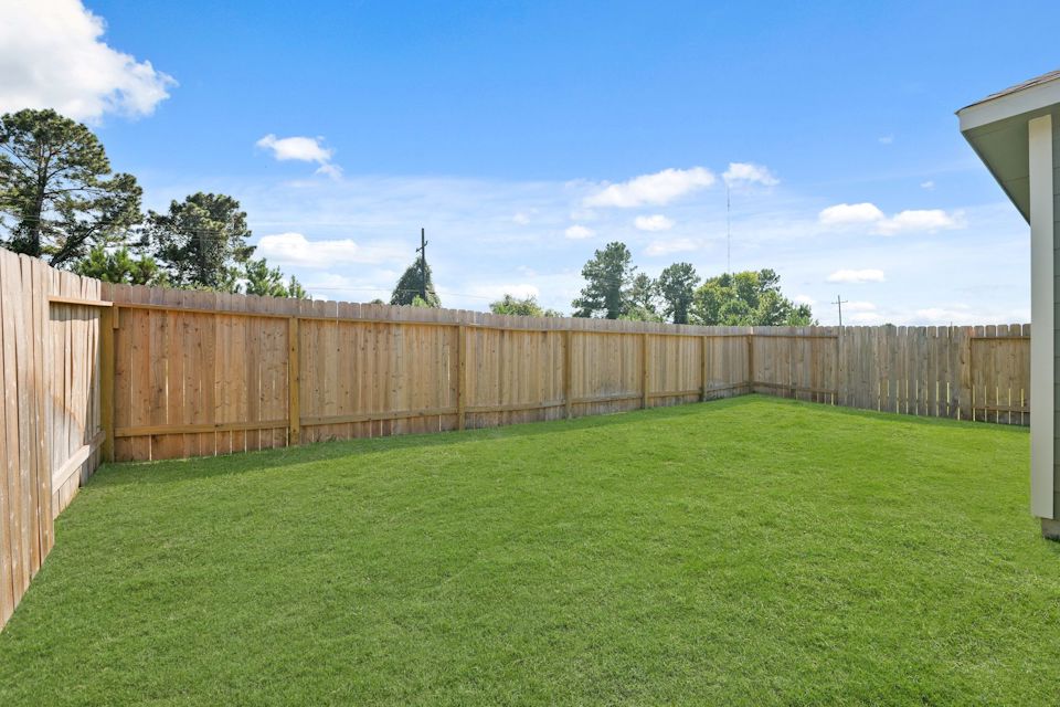 A fenced in yard with a wood fence and trees in the background.