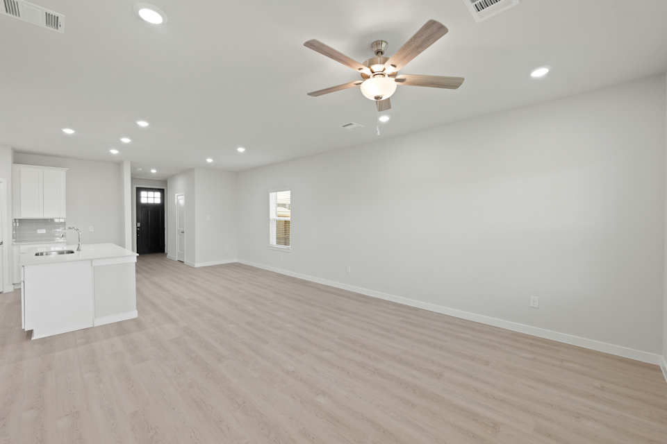 A large empty room with a ceiling fan and a wood floor.